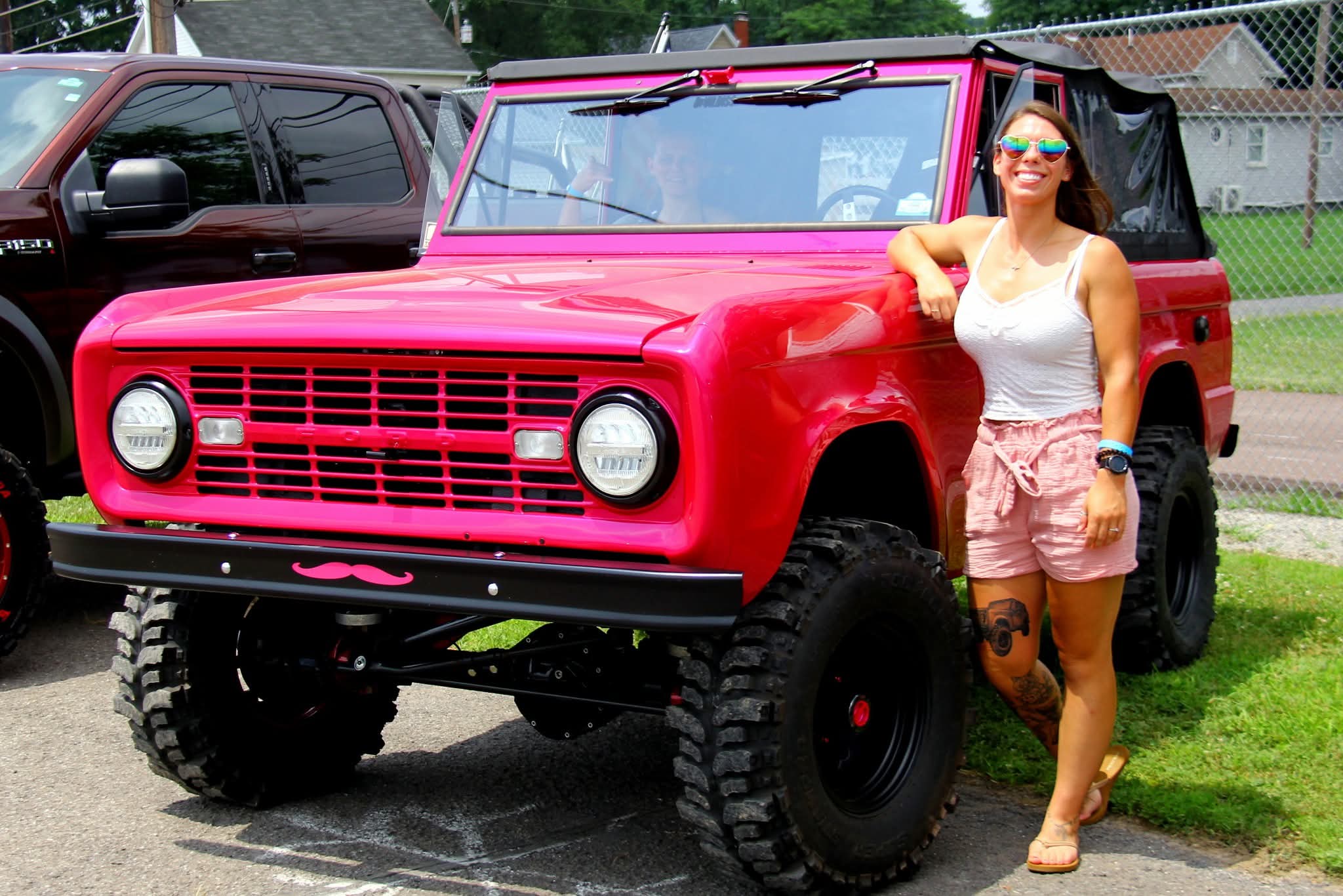 A woman poses, smiling, next to a hot pink Bronco.