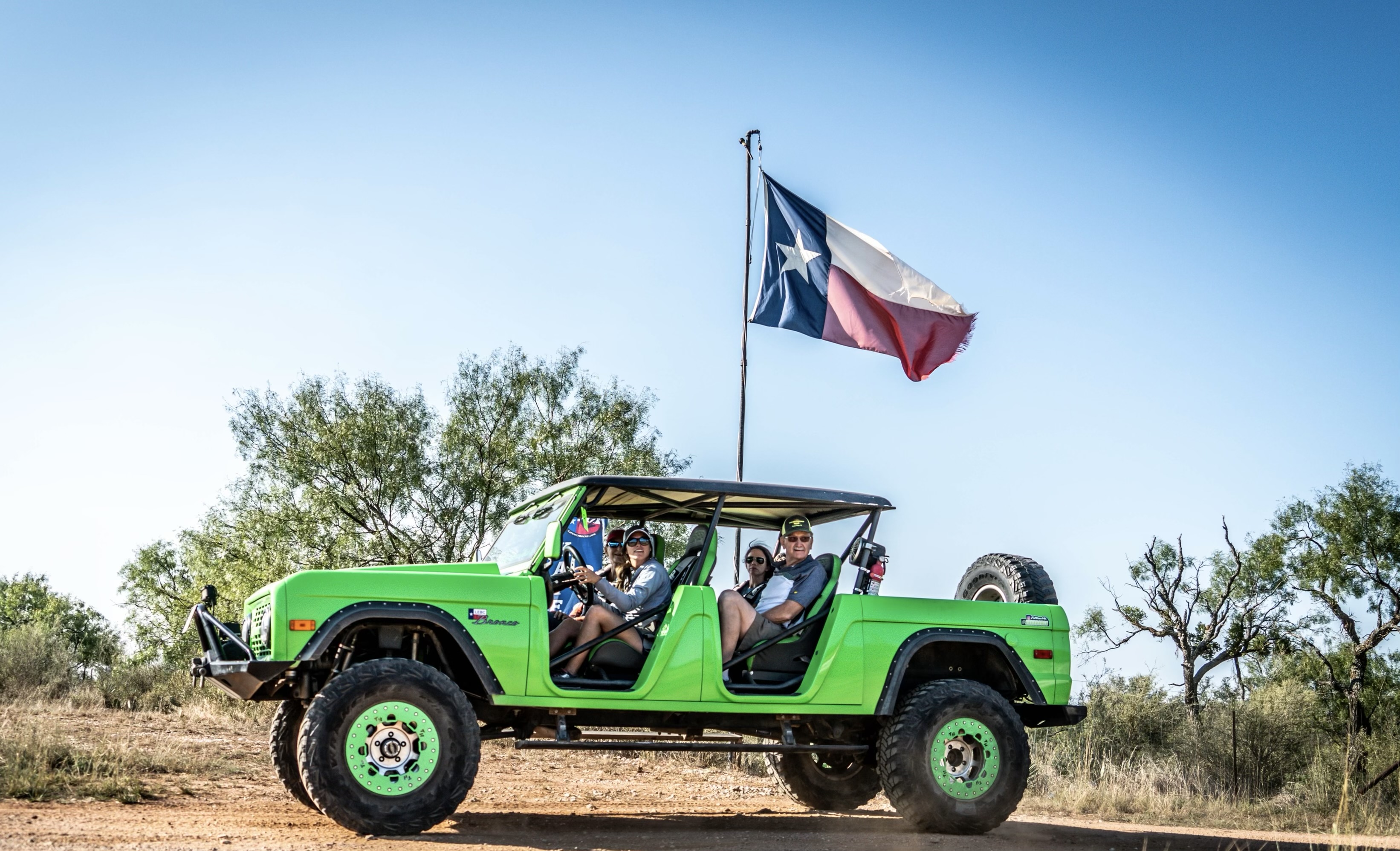 A group of people look at the camera from inside a lime green Bronco with a Texas flag waving on top.