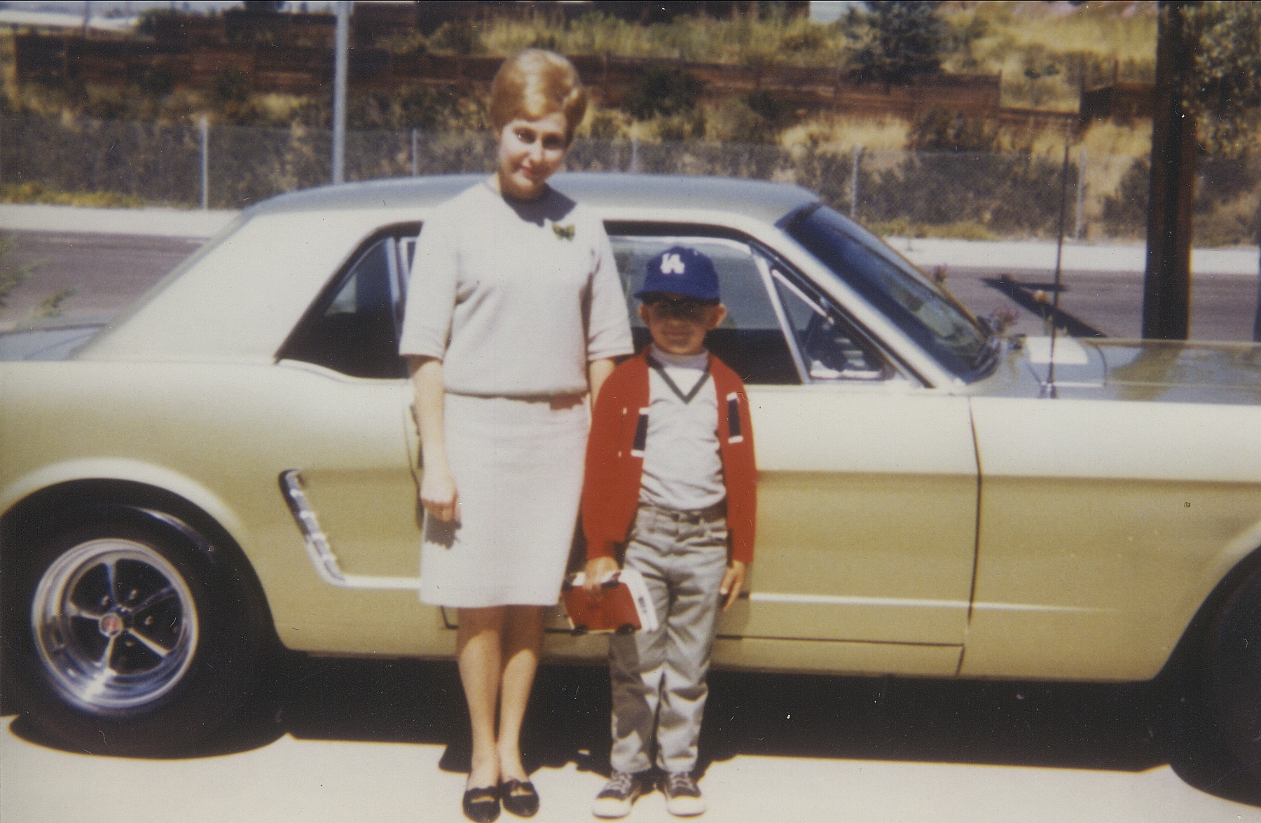 A woman and a young boy stand in front of a Mustang in the 1960s.