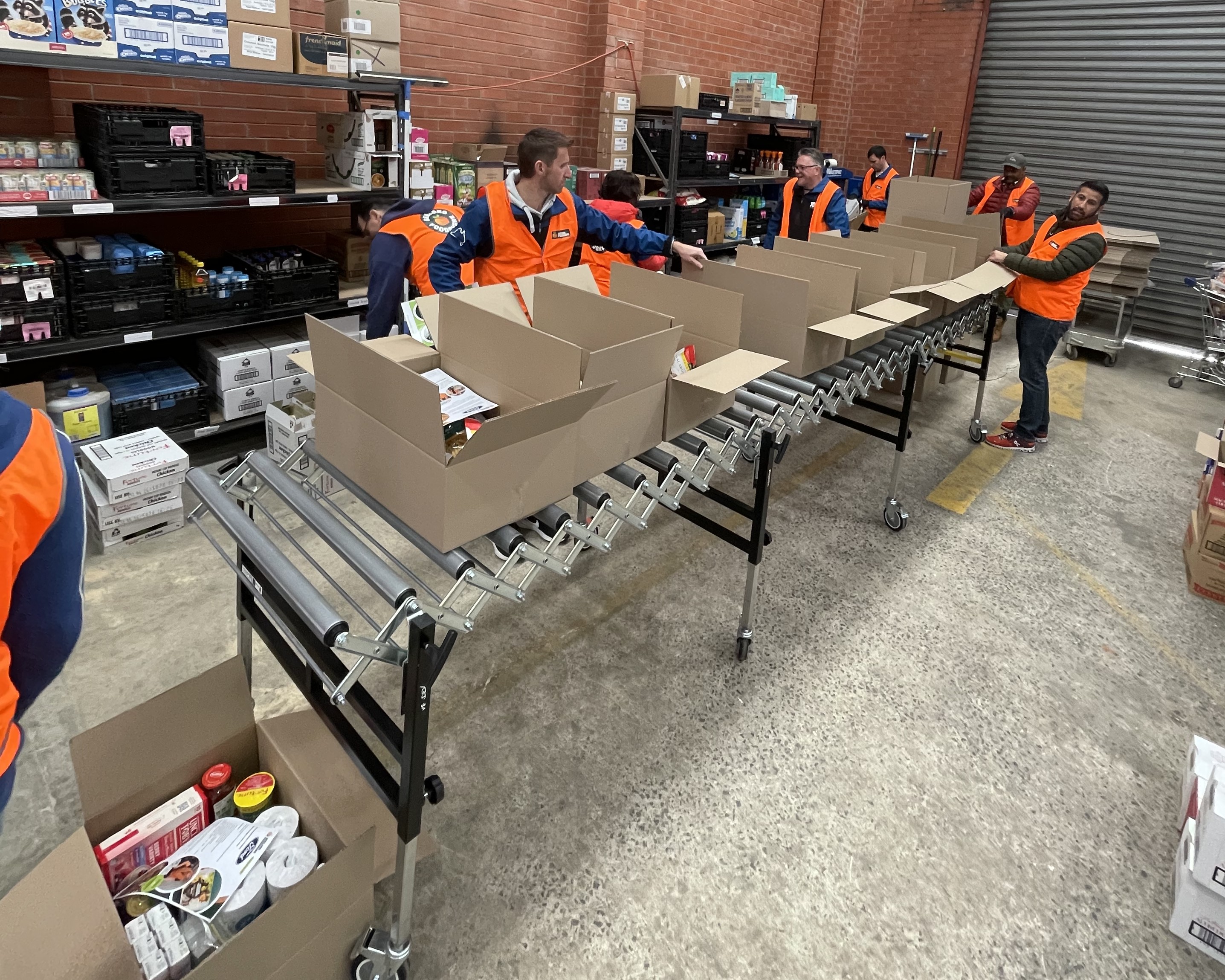 People in orange vests pack boxes on a table.