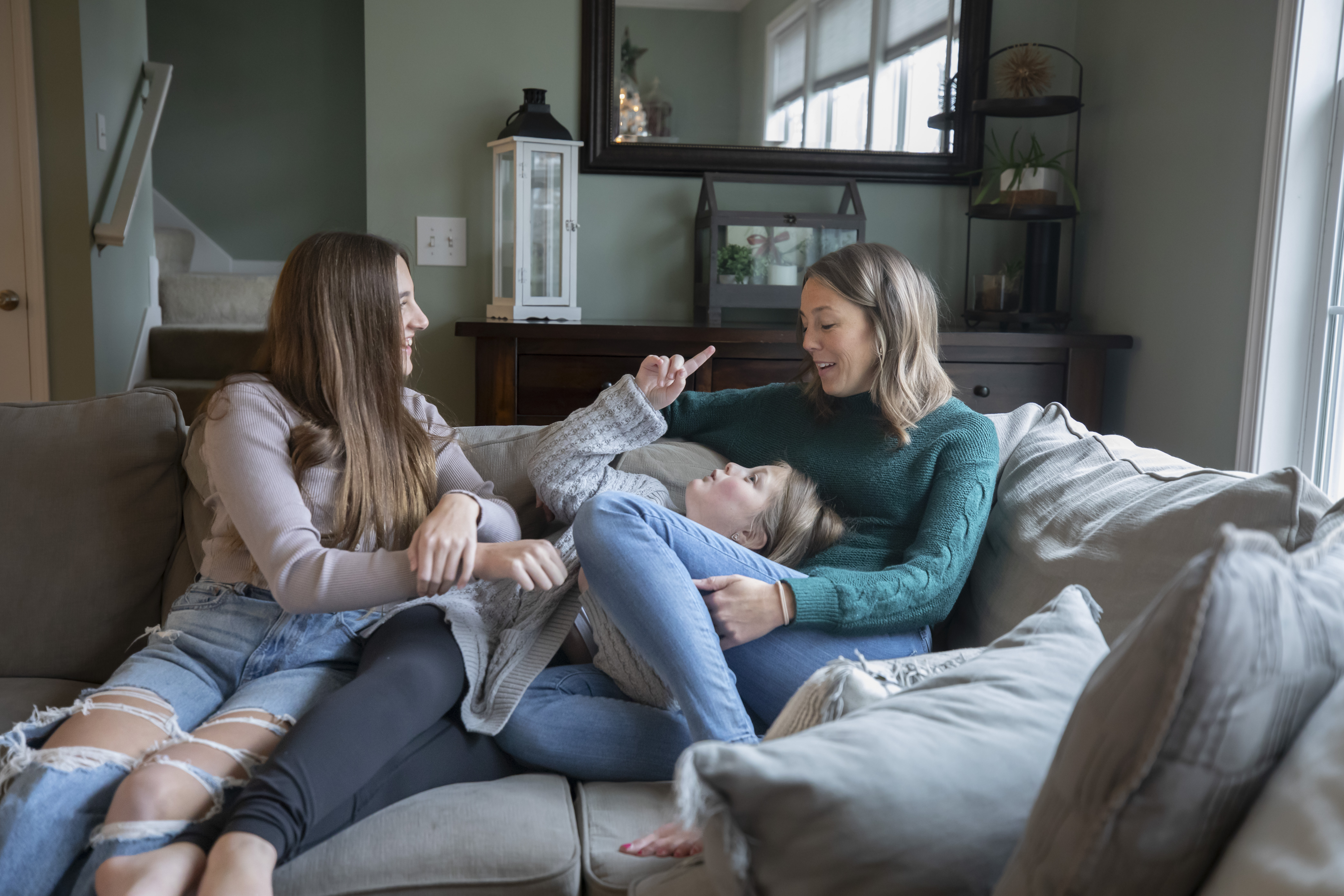 A woman sits on a couch in her living room with her two daughters.