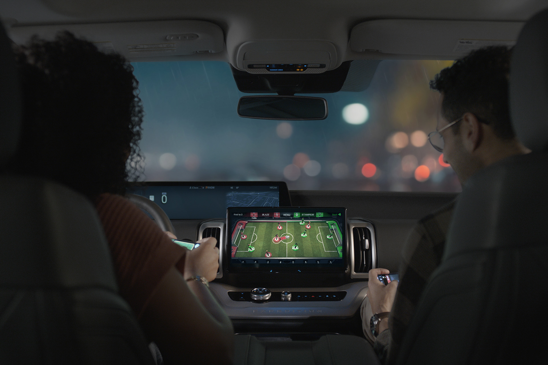 Two people sit in the car and play a game on the console screen.