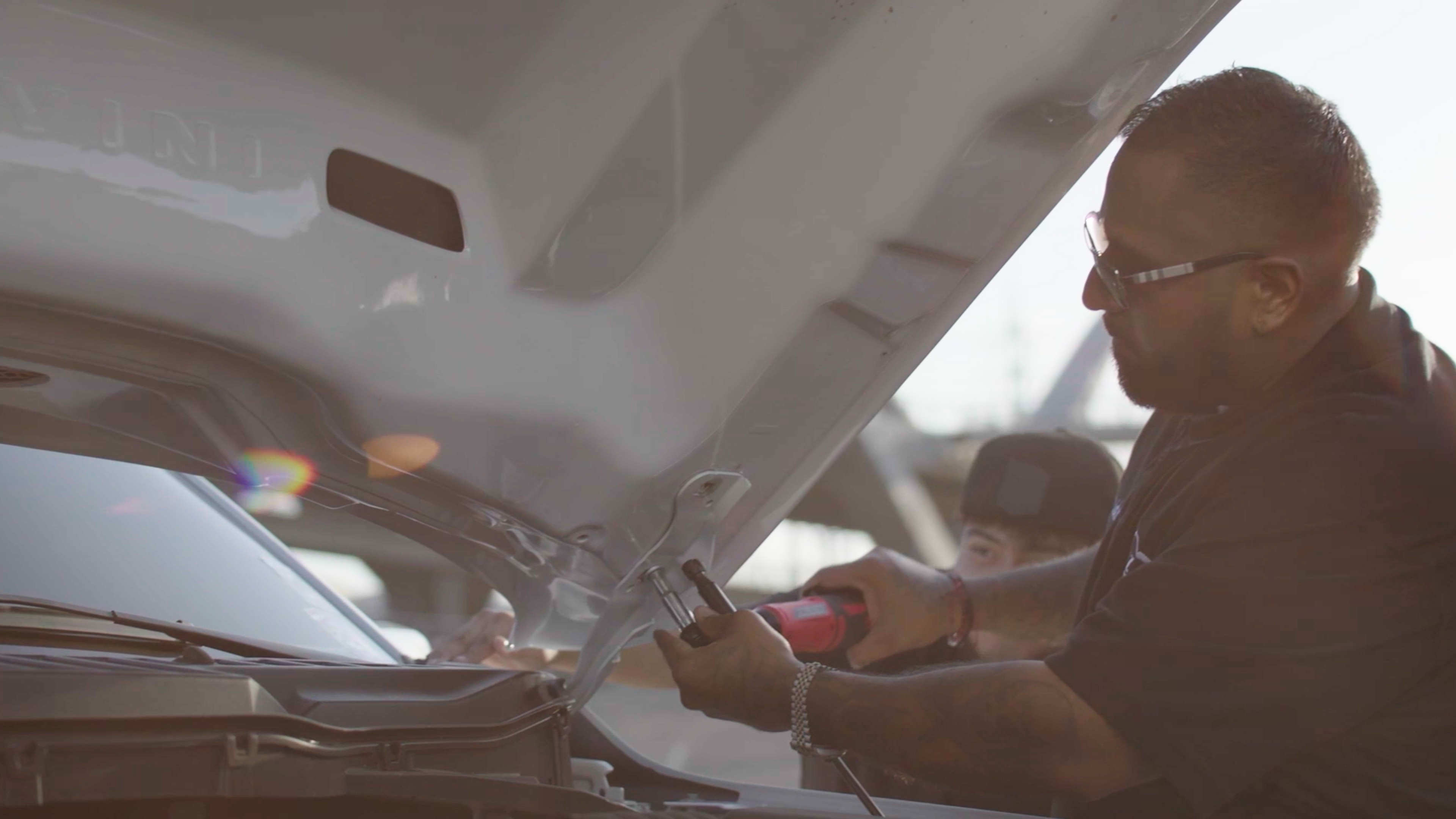 A man works under the hood of a truck.