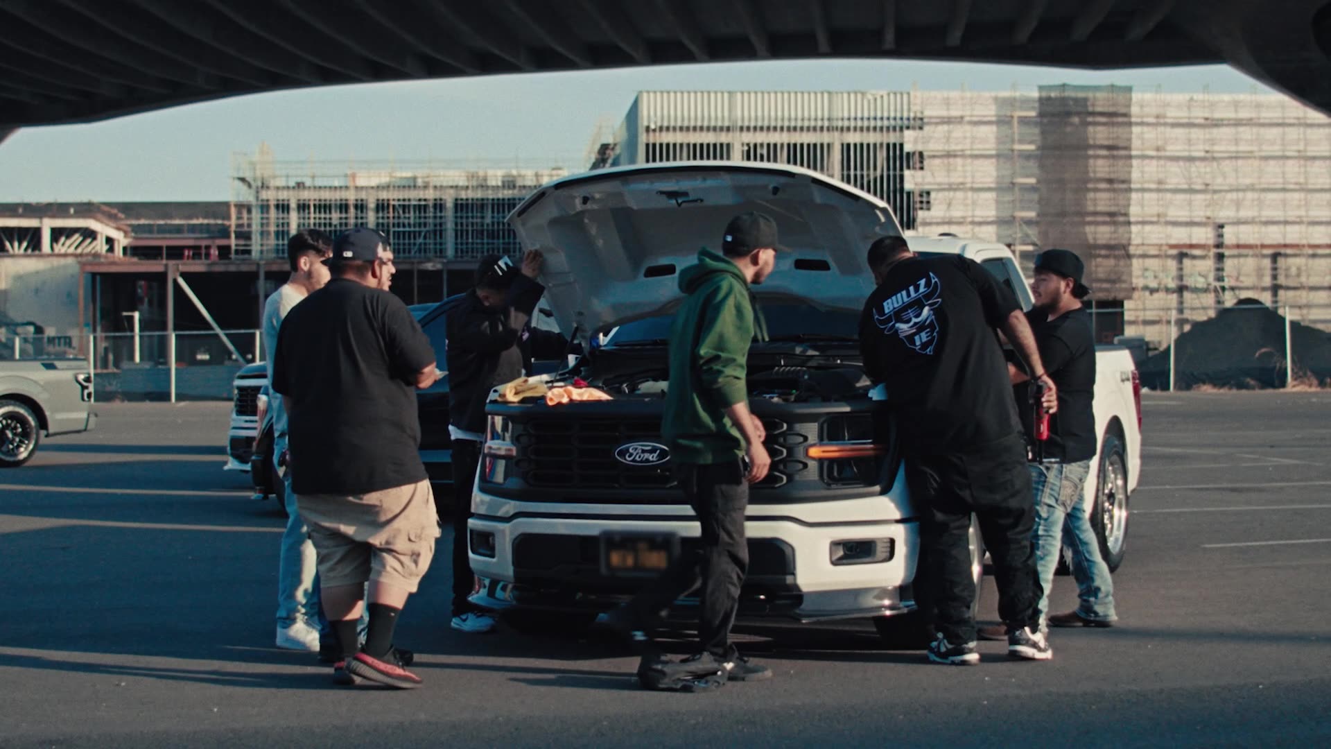 A group of people gather around a street truck to peer under the hood.