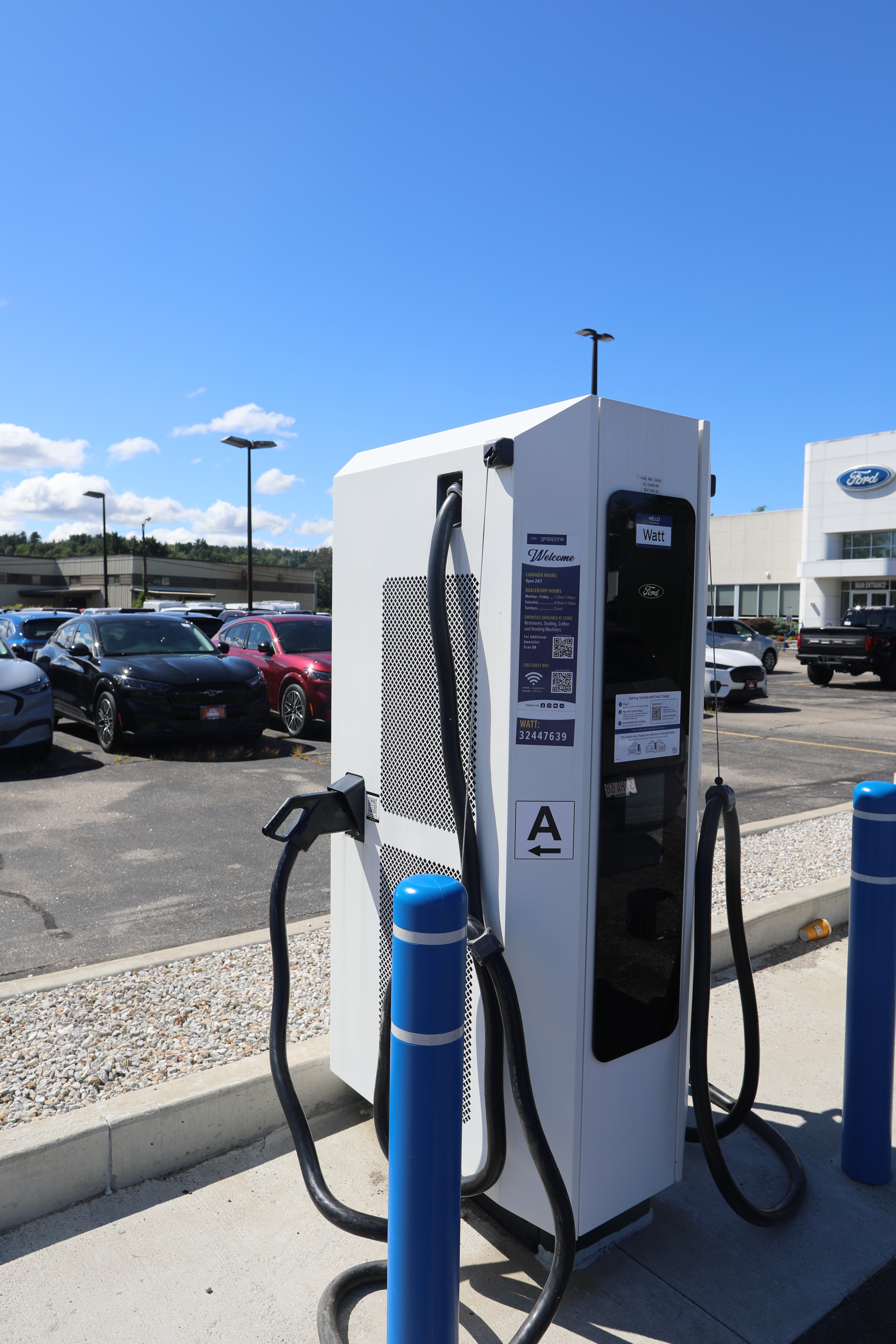 A tall, narrow electric vehicle charger in the parking lot of a Ford dealership.